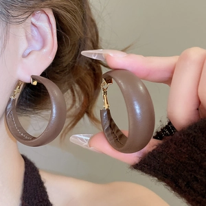 Detailed view of brown leather C-shaped hoop earrings with gold accents on model
