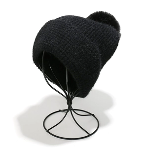 Detailed knit texture of black winter beanie with large faux fur pompom on display stand