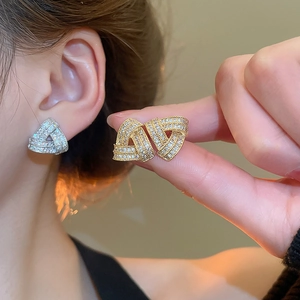 Detail of cross triangle stud earrings with shimmering zircons on model ear