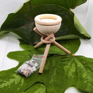 Detail showing a natural wood diffuser stand on green leaves with mixed colored pebbles