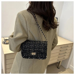 Detail of tweed texture and golden metal chain strap on a black crossbody bag