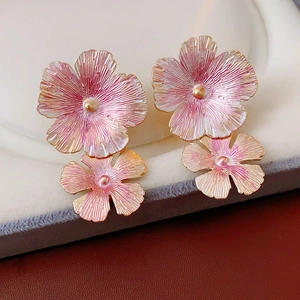 Macro detail of pink and gold enamel flower earrings on a soft jewelry pad display