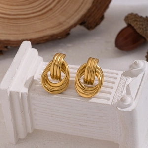 Boucles d'oreilles créoles dorées entrelacées présentées sur un socle blanc décoratif
