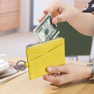 Slim yellow leather coin purse with zipper and key ring shown on a wooden desk