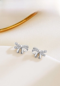 Detail of silver bow stud earrings with micro-set zircons on a ceramic tray