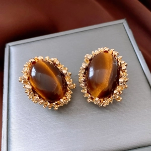 Macro shot of vintage golden earrings featuring oval tiger eye stones and textured edges