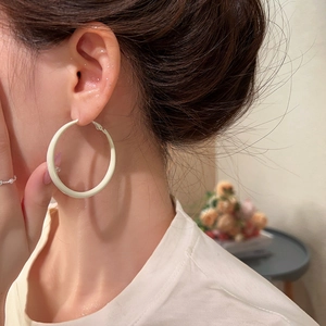 Close-up of a model wearing large cream white enamel hoop earrings in a warm indoor setting