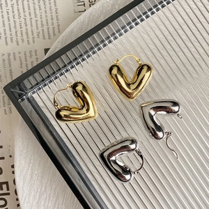 Pendientes de corazón hueco en oro y plata pulidos sobre una bandeja de cristal