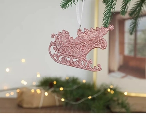 Pink glitter sleigh ornament hanging on a green Christmas tree branch with bokeh lights