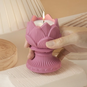 Pink lotus candle holder with burning white candle on a textured beige stone base