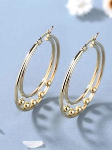 Detail of gold double hoop earrings with metallic beads on light blue background