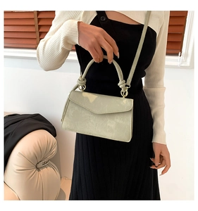 Détail d'un sac à main vert sauge avec finitions dorées et poignée à nœud unique