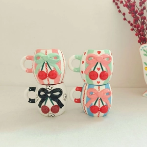 Stack of ceramic cherry and bow mugs in pastel patterns with 3D embossed details