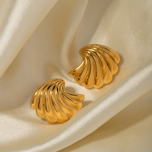 Detailed close-up of golden shell-shaped earrings on beige silk fabric background