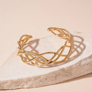 Detail of gold woven mesh bangle with multi-strand twisted metal on white marble base