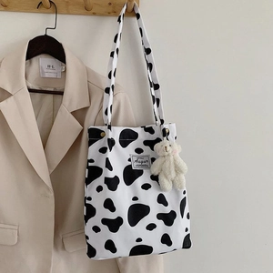 Detailed close-up of a cow print canvas tote bag with a white plush bear keychain