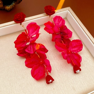 Détail des boucles d'oreilles fleurs en tissu rouge avec perles dans un coffret beige