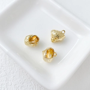 Close-up of three 14k gold-plated textured sea creature pendants in a white ceramic dish