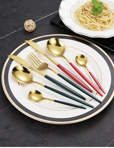 Detail of stainless steel gold cutlery with green and red handles on a marble table