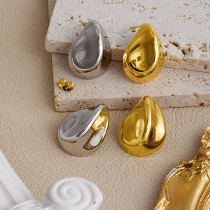 Detailed view of polished gold and silver teardrop earrings on marble display stand