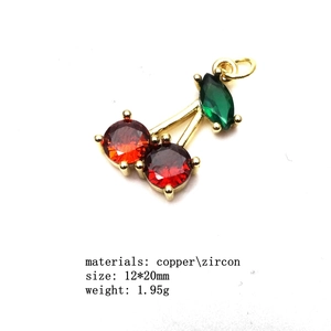 Macro shot of cherry pendant with red and green zircons on polished gold metal base