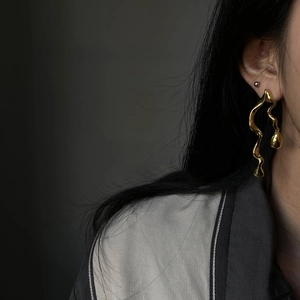 Detailed close-up of gold asymmetrical snake-like drop earrings with waterdrop pendant
