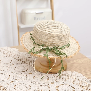 Elegante cappello da sole in paglia di rafia con foglie verdi su supporto di legno