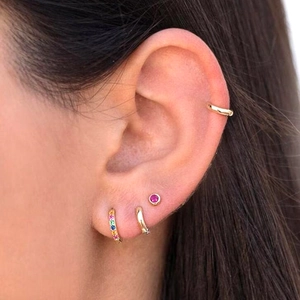 Set of minimalist colorful zircon stud earrings and gold hoops shown on model's ear
