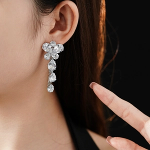 Silver flower earrings with teardrop zircon pendants worn by a model on black background
