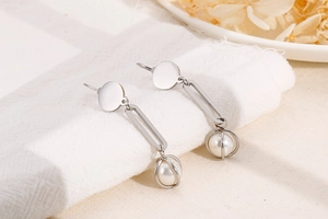 Detail of drop earrings with silver geometric frames and caged white pearls on linen