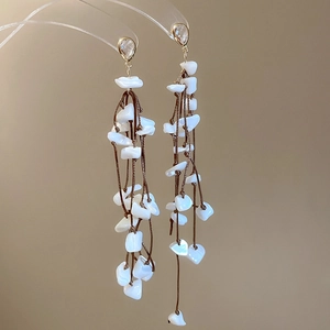 Detail view of handcrafted shell tassel earrings with white stones and braided cord