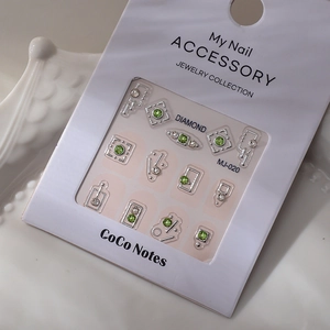 Vue détaillée des bijoux à ongles MJ-020 argentés avec strass verts et blancs sur l'emballage