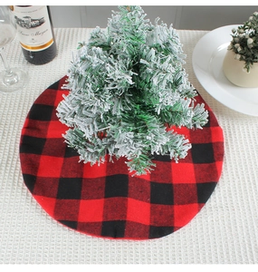 Detail of red and black buffalo plaid Christmas tree skirt under a snowy tree