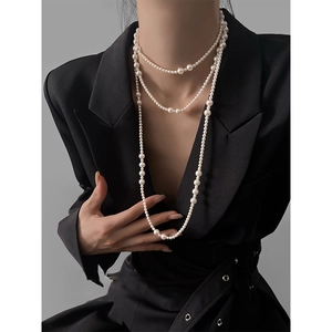 Detail of multi-layered long pearl necklace styled on a black blazer for a vintage look