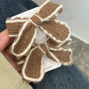 Pair of handmade knit bow hair clips in brown and white wool, shown in hand