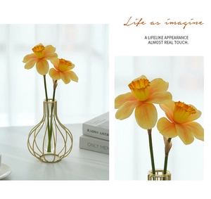 Detail of gold metal frame glass vase with realistic yellow faux daffodils for home decor