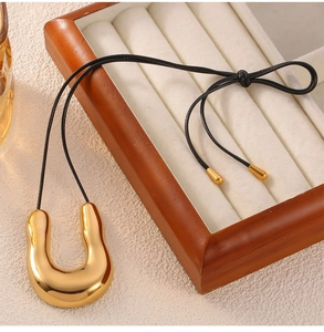 Close-up of a minimalist gold U-shaped pendant on a black cord necklace with a golden clasp