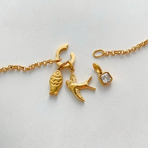 Detail view of gold-plated stainless steel charms featuring a swallow and square crystal.