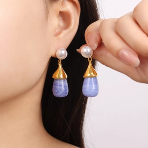 Elegant gold earrings with pearls and purple teardrop pendants worn on ear