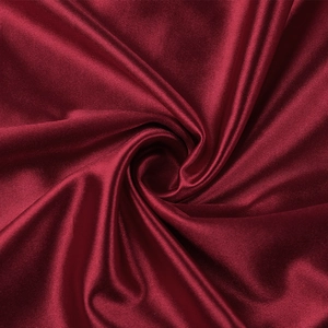 Detailed close-up of wine red satin fabric with elegant spiral drapes and silky luster
