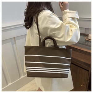Brown canvas tote bag with white stripes shown as a stylish shoulder bag in home setting