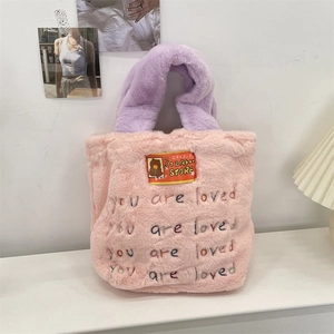 Détail d'un sac cabas en peluche rose avec anses violettes et broderie 'you are loved'