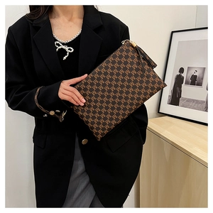 Detail of dark brown envelope clutch bag with M-letter geometric print and tassel charm