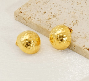 Detailed close-up of 18K gold hammered round stud earrings on elegant beige stone