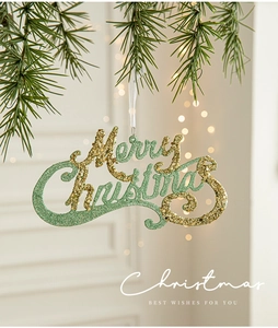 Detail of green and gold glitter Merry Christmas ornament hanging on a pine tree branch