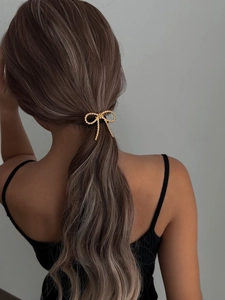 Detail of golden twisted texture bow hair accessory on a woman's low ponytail