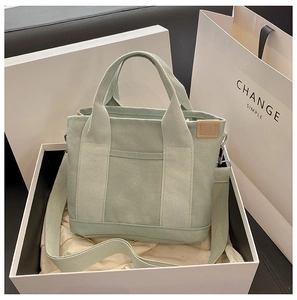 Detail of light green canvas tote bag with shoulder strap in a white minimalist gift box