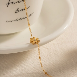Detail of a gold lily of the valley bracelet with tiny rhinestones on a white ceramic cup
