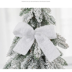 Close-up of a white plush Christmas bow ornament with fuzzy texture on a snowy tree branch