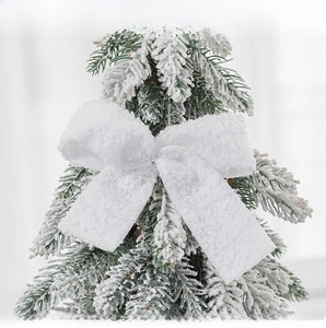 Macro view of a white plush felt bow ornament hanging on a snowy Christmas tree branch